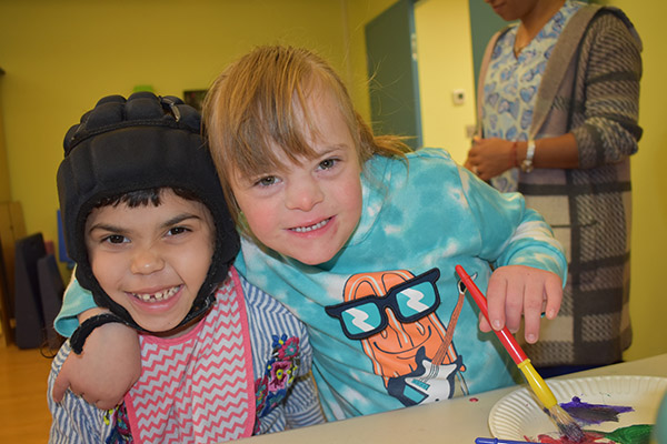 Two elementary students with disabilities hugging while working in art class